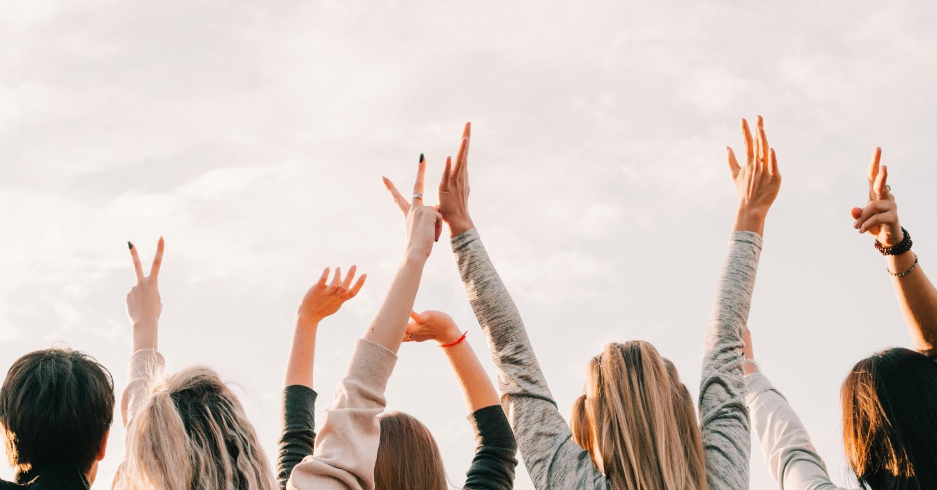 seks unge mennesker som rekker hender oppi været